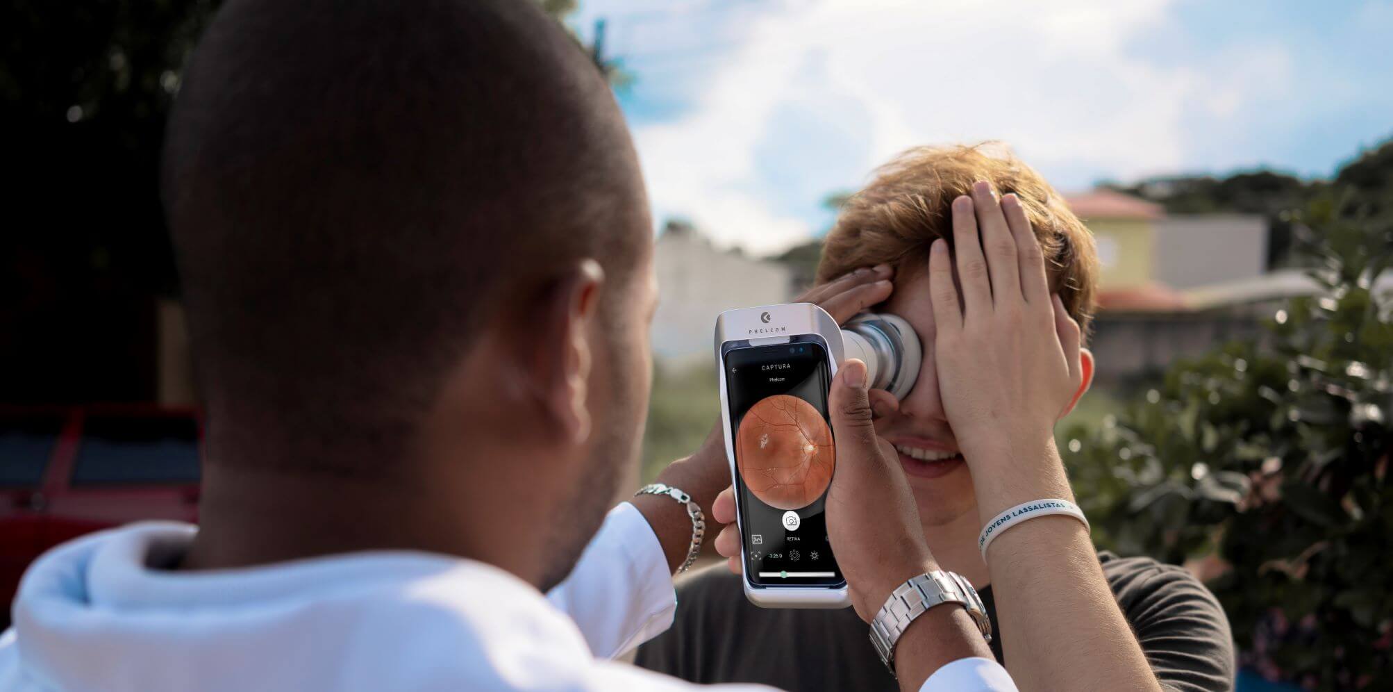Homem jovem sendo examinado por um médico oftalmologista usando o retinógrafo portátil Eyer da Phelcom Technologies.
