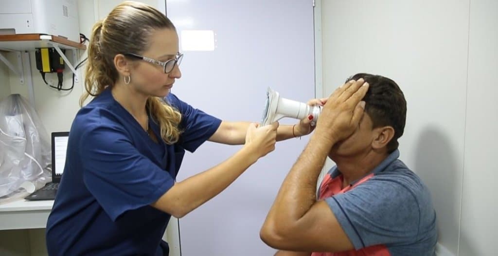 Homem sendo examinado por uma oftalmologista com o Retinógrafo Portátil Eyer da Phelcom Technologies.